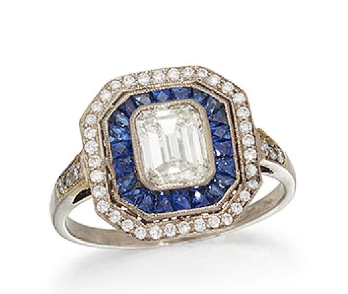 A diamond and sapphire cluster ring, the cut-cornered rectangular diamond centre to a calibre-cut sapphire border and brilliant-cut diamond surround, with brilliant-cut diamond three stone shoulders